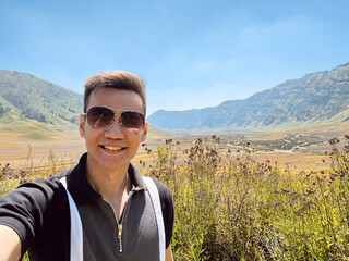 A guy posing in the middle of flower bushes around the mountain valley savannah under a sunny sky. Beauty of nature, mountain and highland photography.