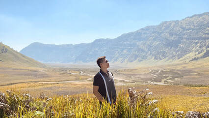 A guy posing in the middle of flower bushes around the mountain valley savannah under a sunny sky. Beauty of nature, mountain and highland photography.