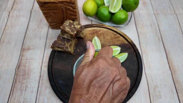 Hands squeeze fresh lime into glass container mixing sweet and citrus notes for a traditional refresher drink papelon con limon