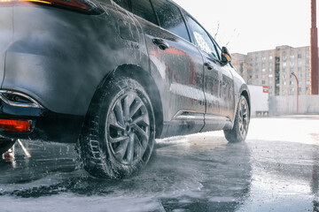 Naklejka premium Washing a dark car with soap and water at a car wash station.