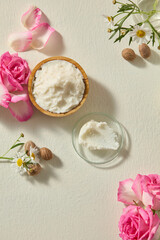 Vertical still life with shea butter chunks, roses and chamomile blossoms arranged neatly. Clean organic beauty concept photo with soft background lighting.