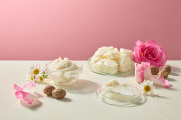 Horizontal arrangement of shea butter surrounded by chamomile flowers and roses. Organic ingredient still life photo with blank space for branding and text.