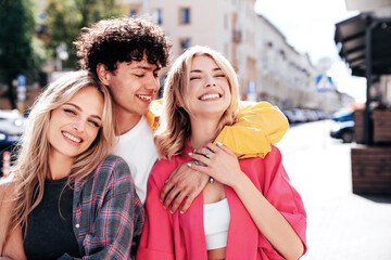 Group of young three stylish friends posing in the street. Fashion man and two cute female dressed in casual summer clothes. Smiling models having fun. Cheerful women and guy outdoors