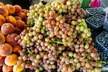 Juicy bunches of red-green grapes surrounded by ripe peaches and boxed blueberries, forming a vibrant and colorful display of seasonal fruit abundance