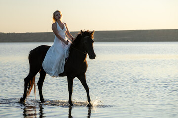 A woman in a white dress rides her horse through Kuyalnik Lake at sunset, the golden light reflecting her serene and timeless beauty.
