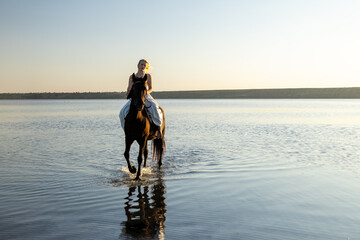 A woman in a white dress rides her horse through the shimmering waters of Kuyalnik Lake at sunset, framed by golden light and stillness.