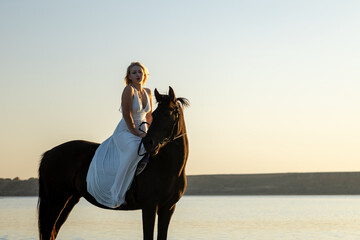 A woman in a white dress sits gracefully on her horse at Kuyalnik Lake during sunset, bathed in warm golden light.