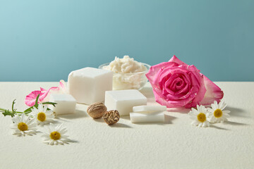 Still life photo showing shea butter with roses and chamomile blossoms styled naturally. Blue background keeps design clean and suitable for branding visuals.