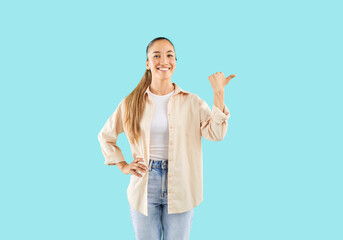 Happy attractive woman showing direction gesture, promoting, advertising friendly smiling, isolated on pastel light pale blue turquoise background, model looking at camera posing for studio portrait