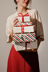 Woman carrying Christmas presents tied with ribbons. Neutral backdrop and sunlight