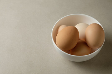 Fresh eggs nestled in a white bowl on a soft kitchen surface