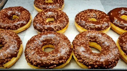 Glazed donuts rings with dark chocolate on a tray in a cafe window on a white background. Dessert food.