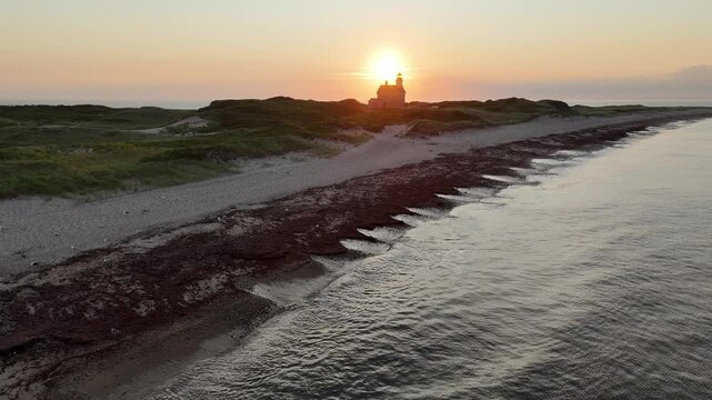 Aerial view of North Light casting a warm glow over the sandy beach and grassy dunes at sunset, New Shoreham, Rhode Island, United States.
