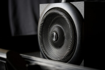 Close-up of modern black professional audio speaker with metal grille in dark studio setup, highlighting details of hi-fi sound technology. Photo