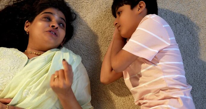 Indian mother son talking while lying on carpet in modern home, spending quality play time together, sharing affection, love, joy, warmth, bonding, parent child relationship, family lifestyle indoors