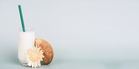 Fresh coconut milk in a glass with a green straw next to a halved coconut