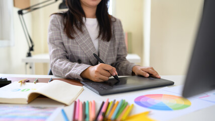 Professional artist working on digital design project with stylus pen and color palette in creative studio workspace