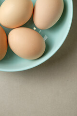 Fresh brown eggs arranged in a teal bowl on a light surface