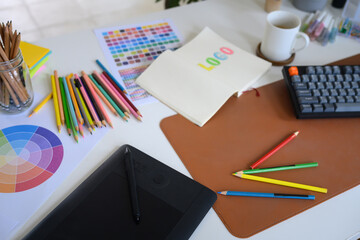 Creative graphic designer workspace with digital drawing tablet, color palette, and notebook for logo design