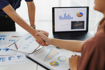 Businesswomen shaking hands over financial business charts and laptop