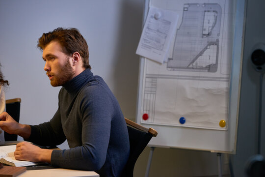 Leading architect explaining main goals for coming month. Confident bearded man in gray turtleneck sitting at desk and talking to his colleagues - Powered by Adobe