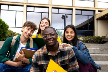 Happy multi-ethnic students sitting on university steps holding notebooks and smiling
