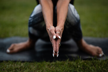 Yoga instructor performing sukhasana pose on grass with hands joined in prayer position