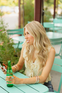 Blonde woman relaxing outdoors holding phone and drink