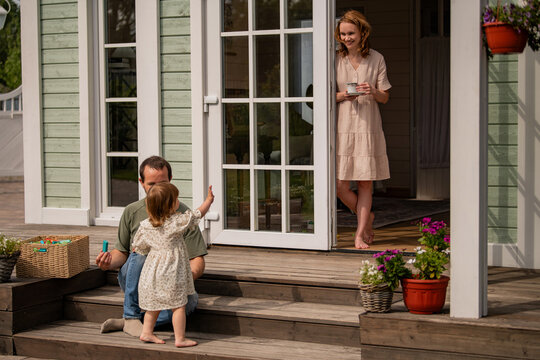 family with child is relaxing sitting on porch of country house.