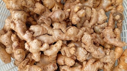 A close-up image of fresh ginger roots displayed in a white basket. The brown rhizomes have a rough texture and natural shapes, often used as a spice and traditional herbal medicine. Ginger is widely 
