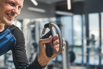 Smiling happy athlete training with expander to build forearm muscles and improve grip strength. Mature athlete using grip trainer with determination in bright gym interior