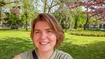 Smiling woman with European features amidst cherry blossoms, celebrating Hanami's fleeting beauty, echoes Vernal Equinox renewal April 5, 2025, Barcelona, Spain