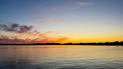 Sunset paints the sky in swirling tangerine and indigo, reflecting tranquility on water, invoking Serenity Day, Midsummer Festival