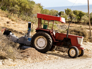 Tractor with wood chipper, red agricultural tractor equipped with a wood chipper machine, processing branches and logs into wood chips. Concept of farming, forestry, agriculture, and rural work.