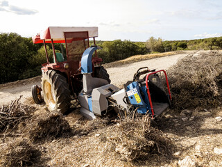 Tractor with wood chipper, red agricultural tractor equipped with a wood chipper machine, processing branches and logs into wood chips. Concept of farming, forestry, agriculture, and rural work.