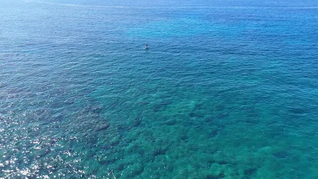Aerial view of a lone paddleboarder gliding across turquoise waters, a serene dance between human and ocean, captured in a vibrant seascape, Hawi, Hawaii, United States.