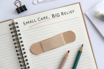 Adhesive bandage lying on a notebook with the quote 'Small Care, Big Relief'