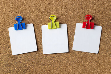 Colorful binder clips hold blank white note cards on a cork bulletin board, creating a neat, minimal workspace scene with plenty of copy space