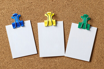 Colorful binder clips hold blank white note cards on a cork bulletin board, creating a neat, minimal workspace scene with plenty of copy space