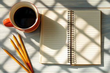 Top-down view of an open lined notebook with a cup of black coffee and pencils on a wooden desk, illuminated by warm morning sunlight that casts soft shadows