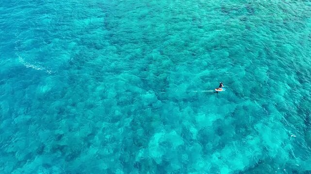 Aerial view of a lone surfer gliding across the crystalline turquoise waters, a mesmerizing blend of textures and tones, Hawi, Hawaii, United States.