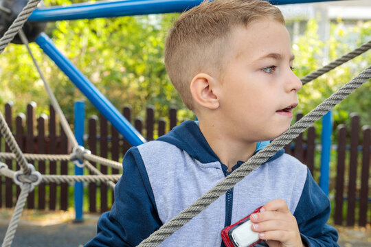Cute boy with a modern haircut playing and climbing on a rope net structure at an outdoor playground, looking away, close-up