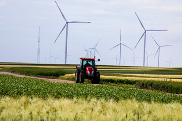 Red tractor traverses verdant fields under towering wind turbines, whispering echoes of World Biodiversity Day and Renewable Energy Appreciation April 5 2025, Barcelona, Spain