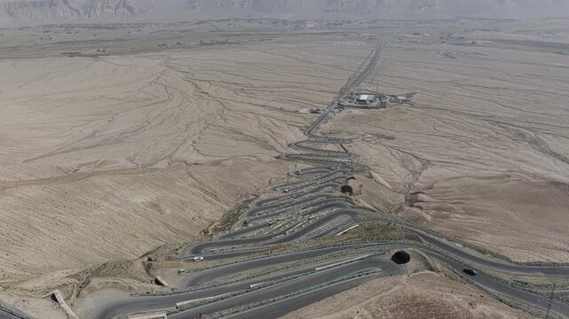 Aerial view of the winding Panlong Ancient Road cutting through the stark, arid landscape, a ribbon of asphalt amidst the muted tones of the terrain, Panlong Ancient Road, China.