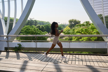 Young sporty woman running on modern bridge in urban park