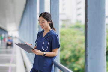 Young female doctor writing notes on clipboard in hospital corridor