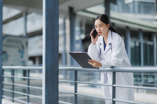 Female doctor talking on phone and reading medical report in hospital corridor - Powered by Adobe