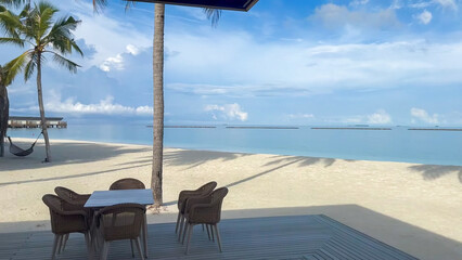 Dining area on a wooden deck overlooking the white sandy beach and calm, clear turquoise sea