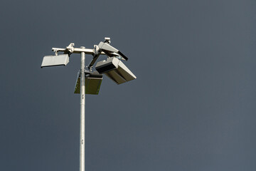A tall street light is equipped with multiple cameras and lighting units, showcasing modern urban surveillance technology against a dramatic cloudy sky.
