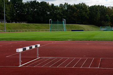 Obraz premium A clear view of a hurdle positioned on a red track at an athletic facility. The green grass field features trees in the background, providing a peaceful training atmosphere.